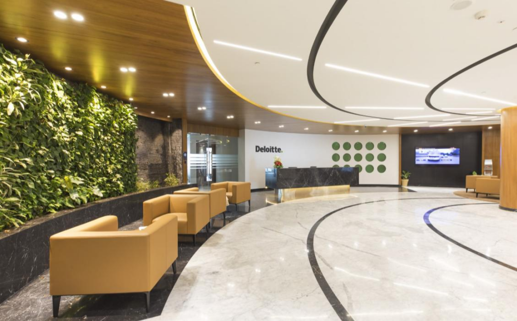 . Reception lobby: sweeping black curved ceiling band on cream soffit, polished marble floor with curving inlay, green living wall, Deloitte reception desk, tan leather lounge chairs.